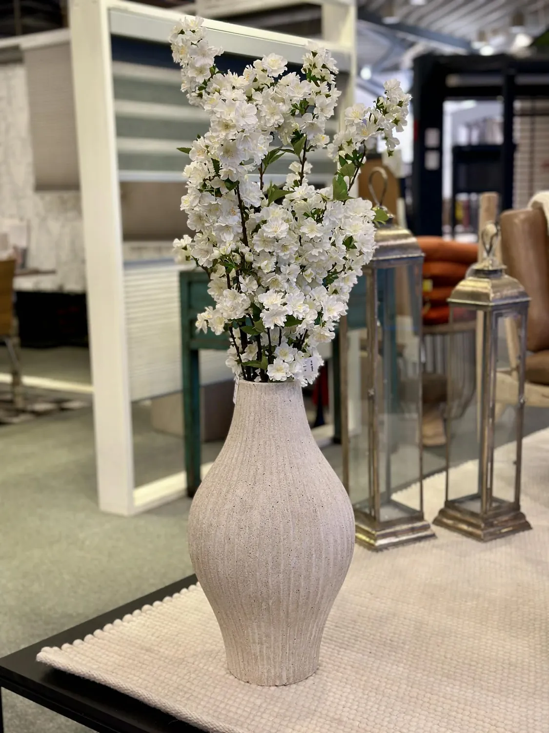 Høj vase med hvide blomster på spejlkonsol i showroomet